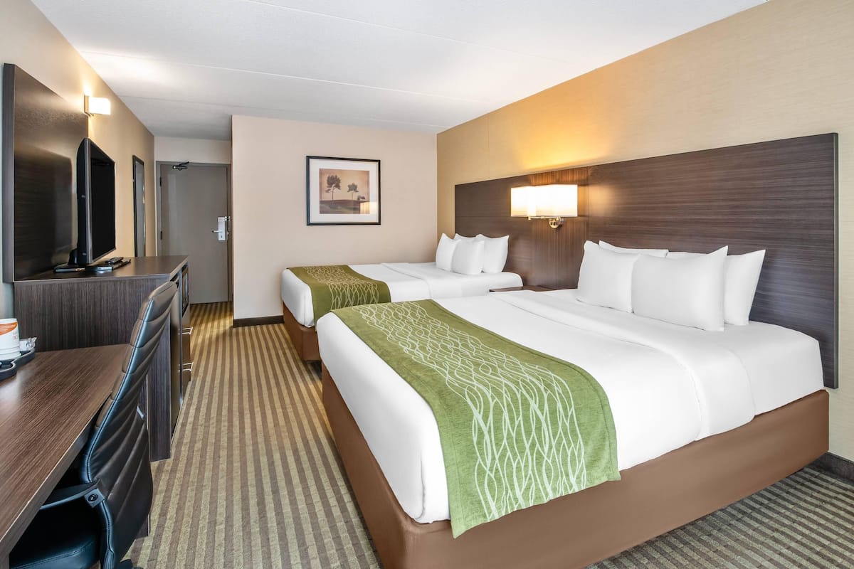 A hotel room with two beds, a desk with a flat-screen TV, a framed picture on the wall, and a lamp on the nightstand.