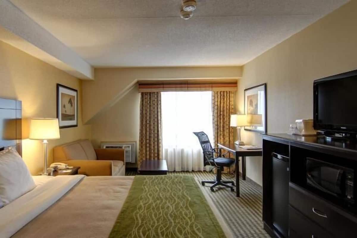A hotel room with a bed, desk, chair, television, and a window with curtains.