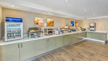 Ein moderner Frühstücksbereich mit einer Selbstbedienungs-Kühlschrank, Kaffeeautomaten und einer Auswahl an Speisen.