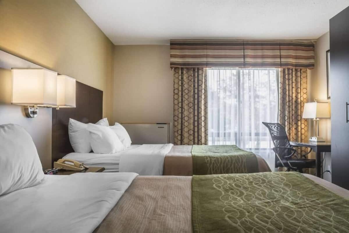 A hotel room with two beds, a desk, a chair, and a window with curtains.