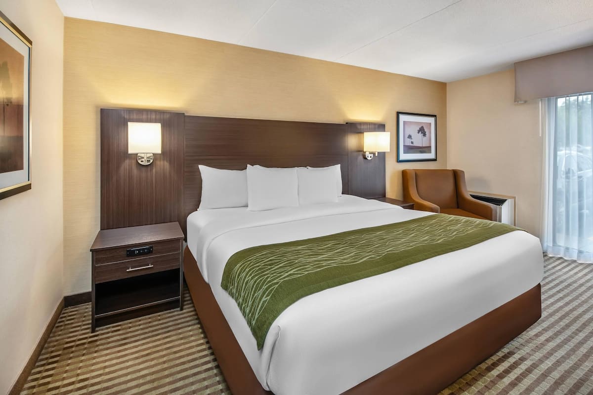 A hotel room with a large bed, two bedside tables, a chair, and a window with curtains.