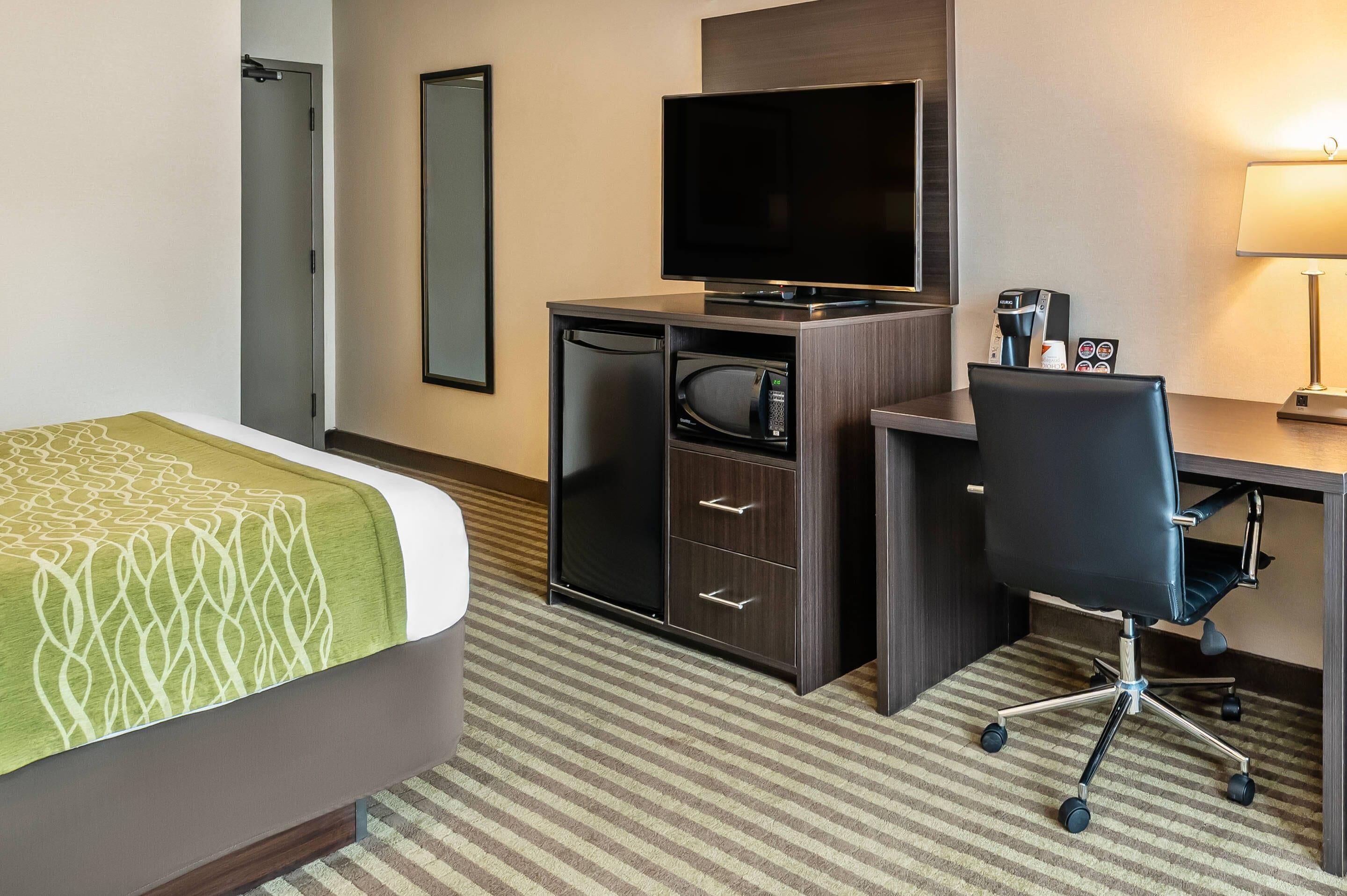 A hotel room with a bed, a desk with a computer, a television, a microwave, and a coffee maker.