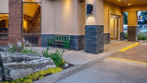A hotel entrance with a stone facade, a green bench, and a staircase leading to the interior.