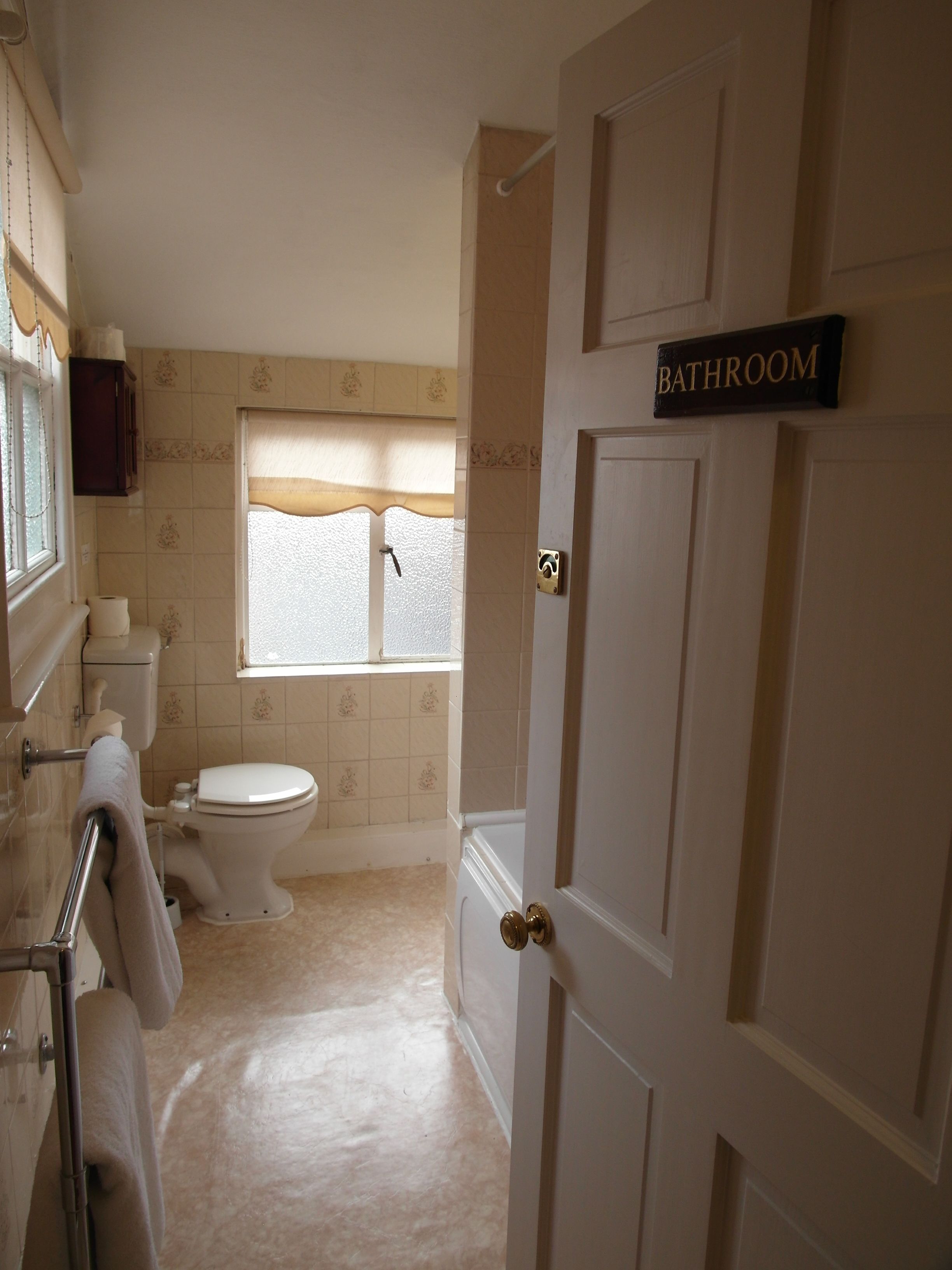 A bathroom with a toilet, a sink, and a window. There is a sign above the door that reads "BATHROOM".