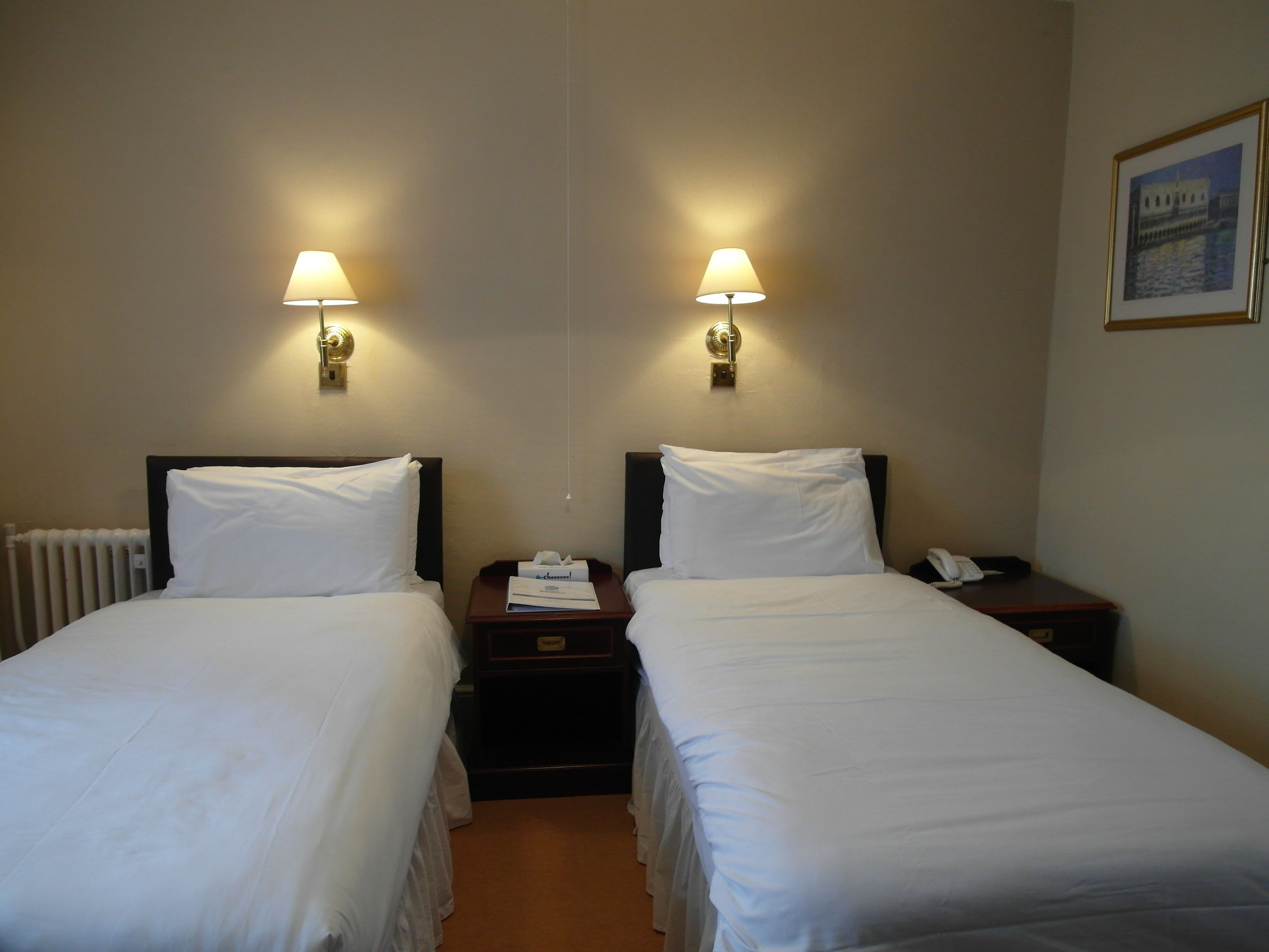 A hotel room with two single beds, each with a nightstand, a lamp, and a telephone.