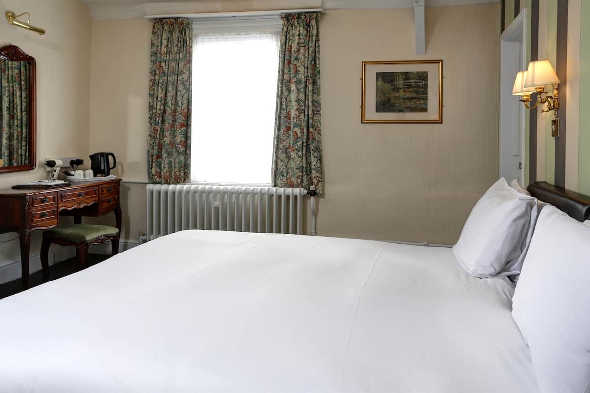Une chambre d’hôtel avec un grand lit, un bureau avec une chaise, un radiateur et une fenêtre avec des rideaux.