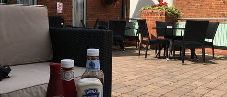 Una mesa con una porción de papas fritas, botellas de salsas y saleros y pimenteros frente a un edificio con un letrero que dice 'GEORGE HOTEL'.