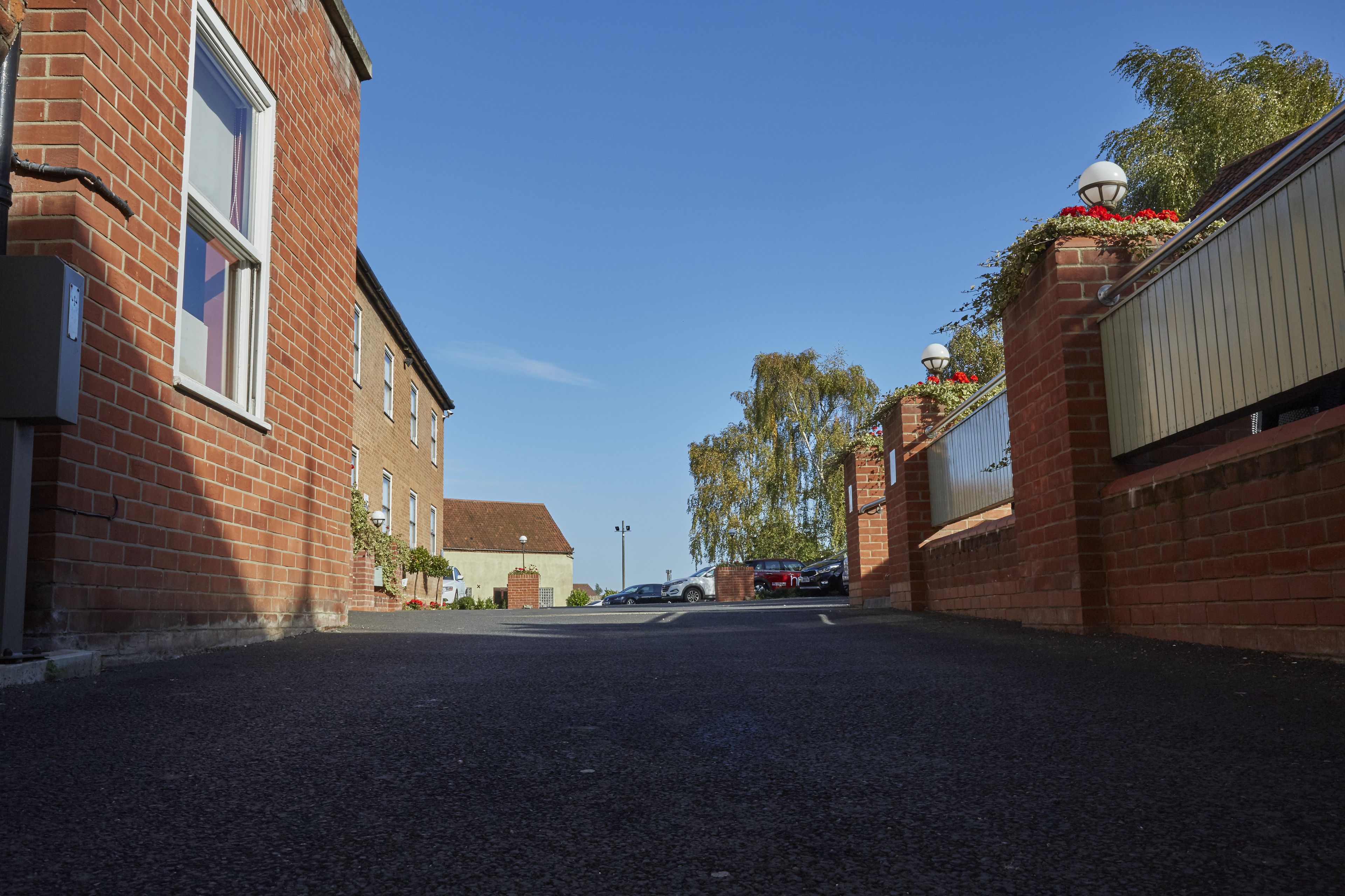 A residential street with brick houses, a clear sky, and a parked car.