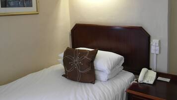 A hotel room with a bed, a nightstand with a telephone, a painting on the wall, and a wooden headboard.