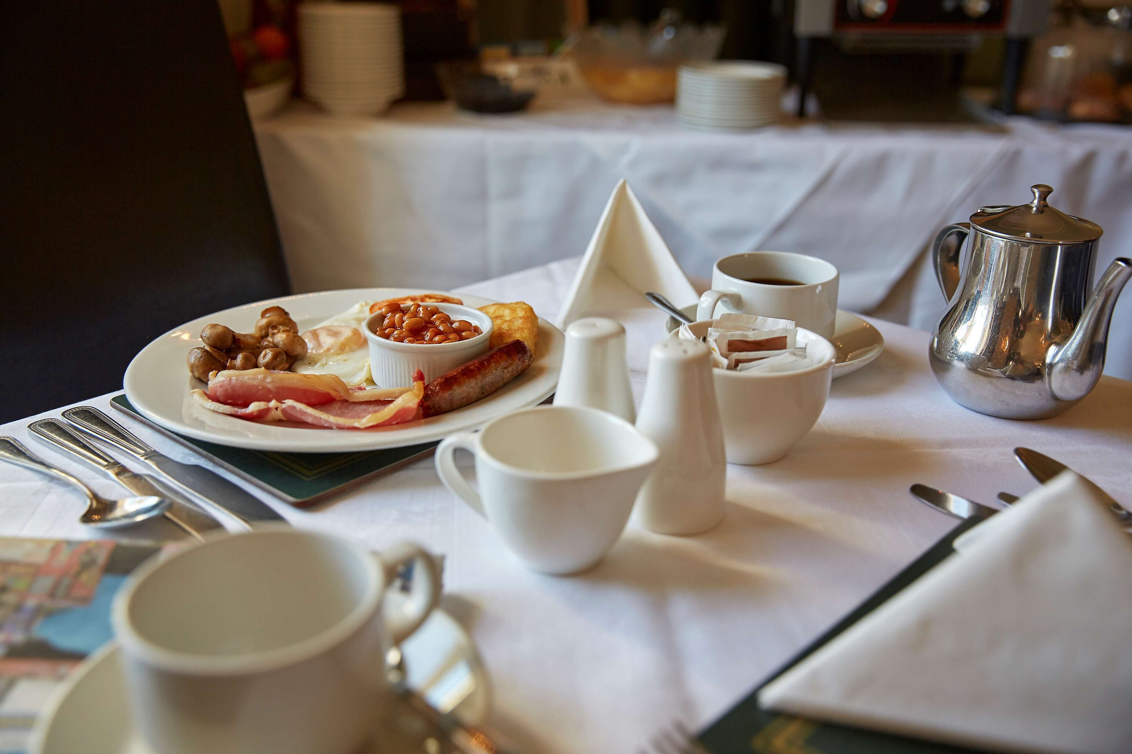 A breakfast setting with a plate of food, a teapot, cups, and cutlery on a table.