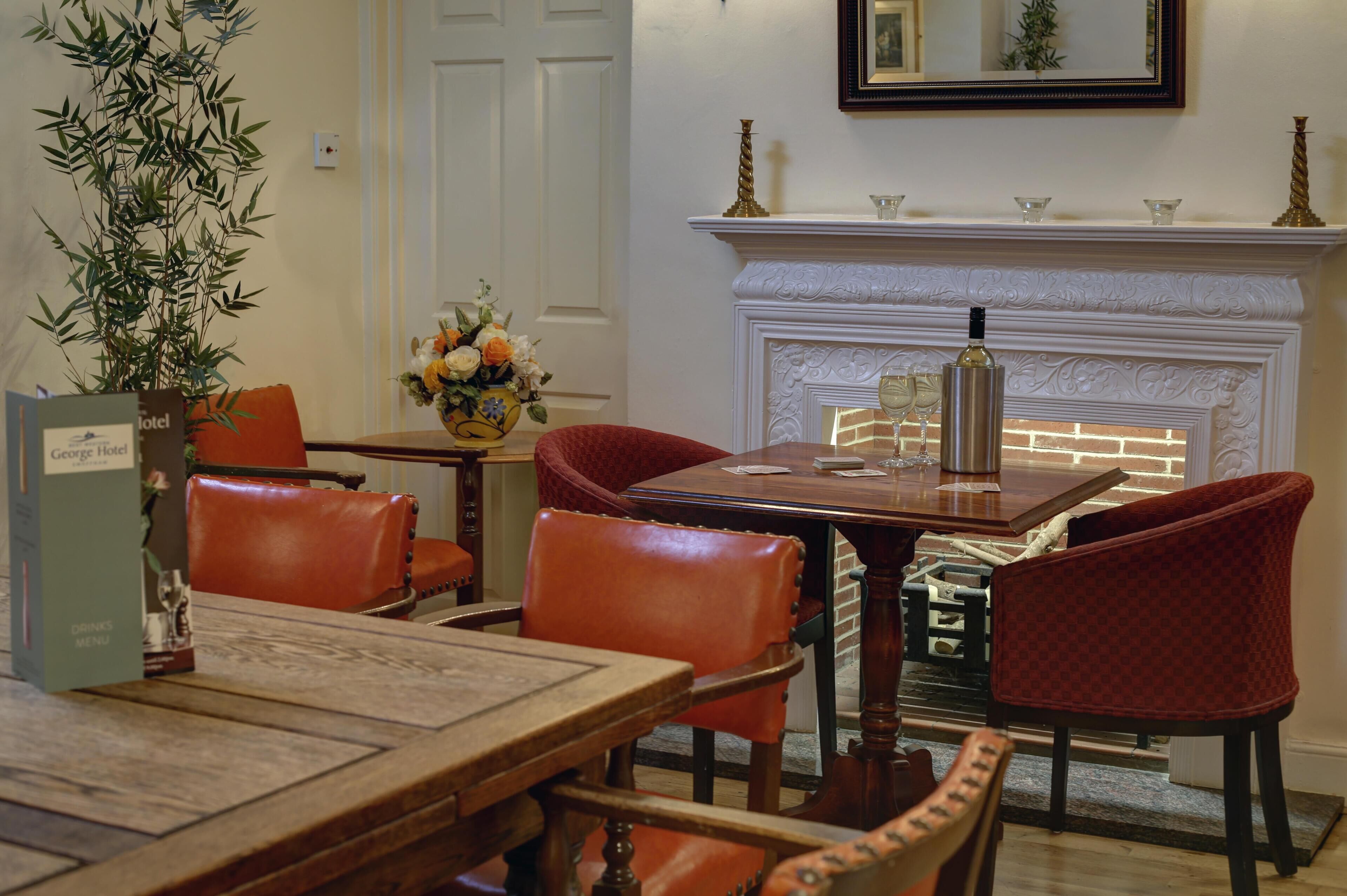 A dining area with a wooden table and leather chairs, a vase with flowers, and a fireplace with a mantel.