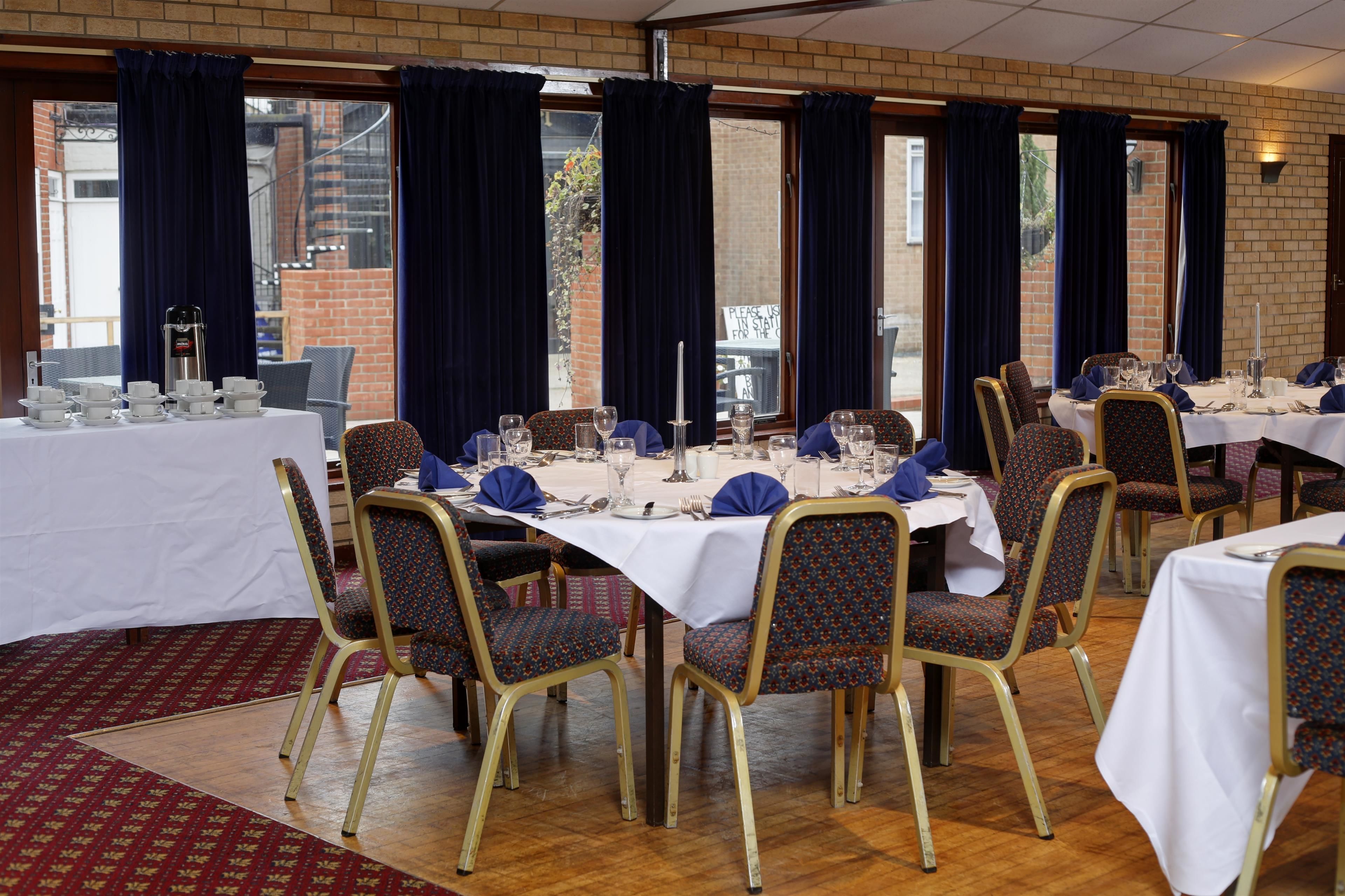A dining area with tables set for a meal, chairs with patterned upholstery, and a brick wall in the background.
