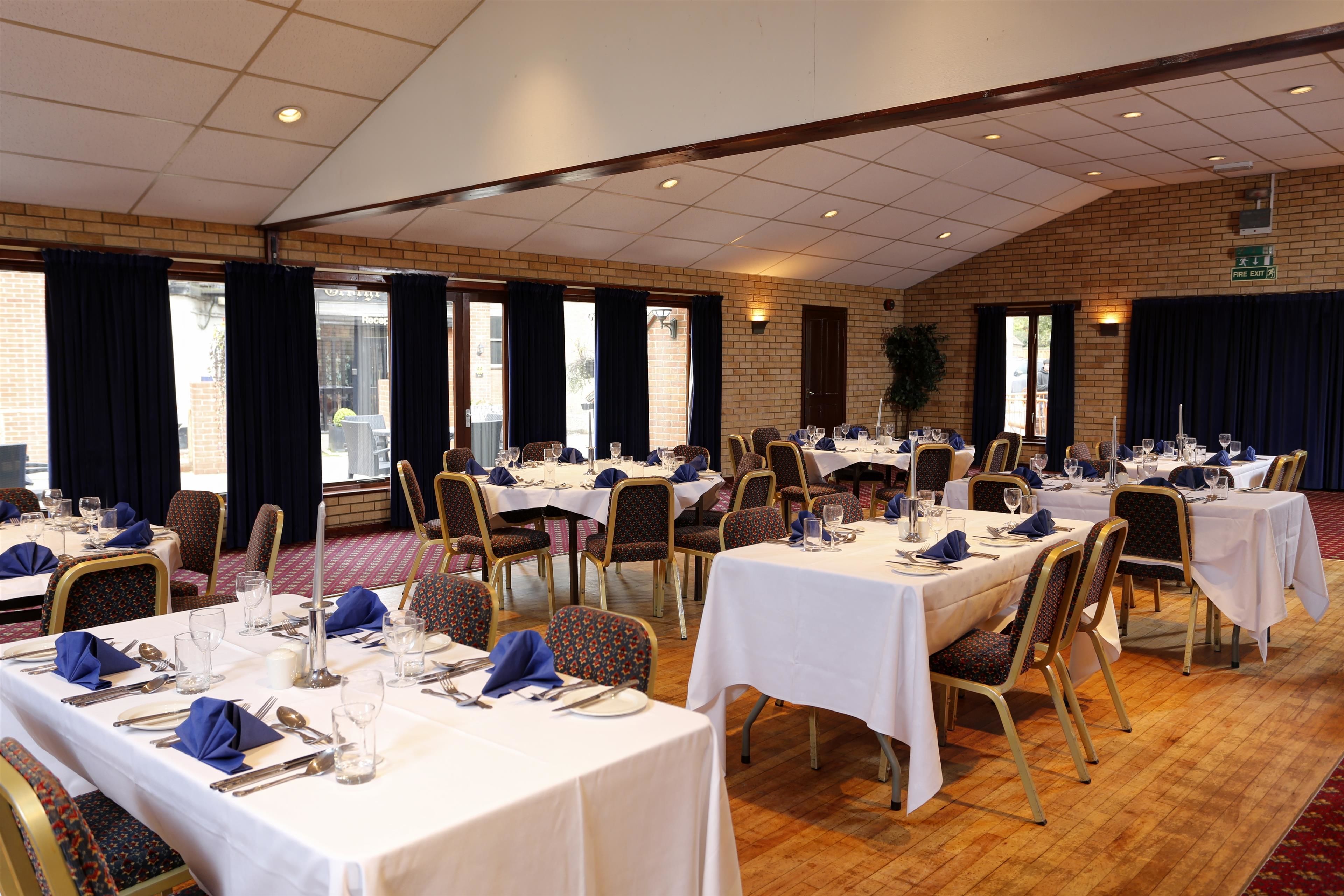 A banquet hall with multiple round tables set for dining, each with white tablecloths, chairs, and dining utensils.