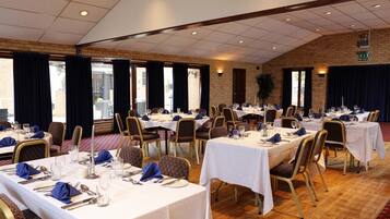 A banquet hall with multiple round tables set for dining, each with white tablecloths, chairs, and dining utensils.