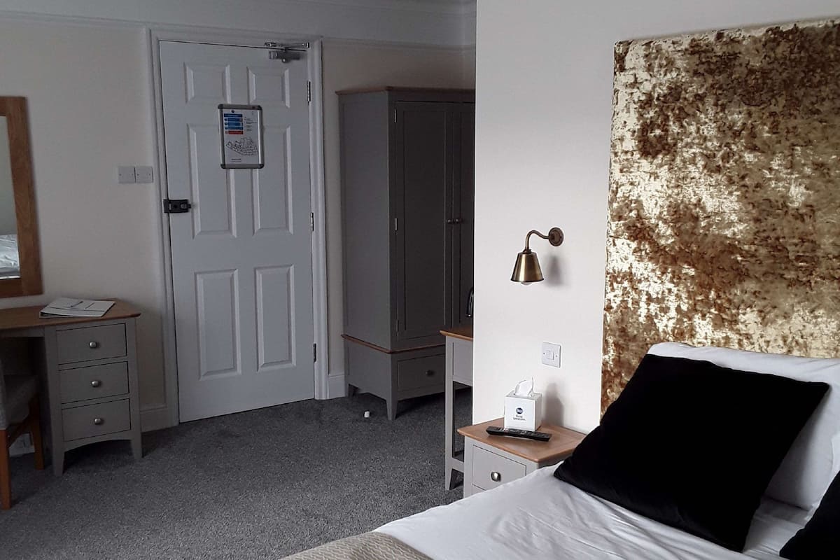 Une chambre d’hôtel équipée d’un lit, d’un bureau, d’une armoire, d’un miroir et d’une lampe fixée au mur.
