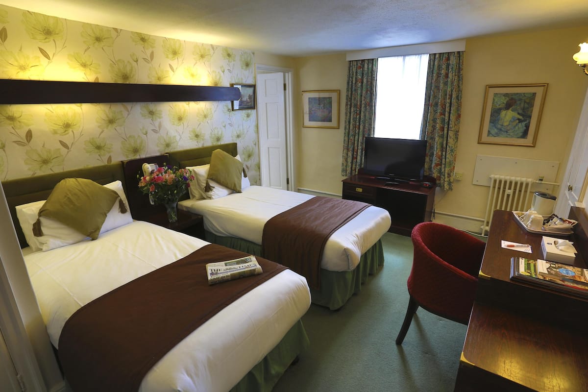 Une chambre d’hôtel avec deux lits, un bureau, une chaise, une télévision et une fenêtre avec des rideaux.