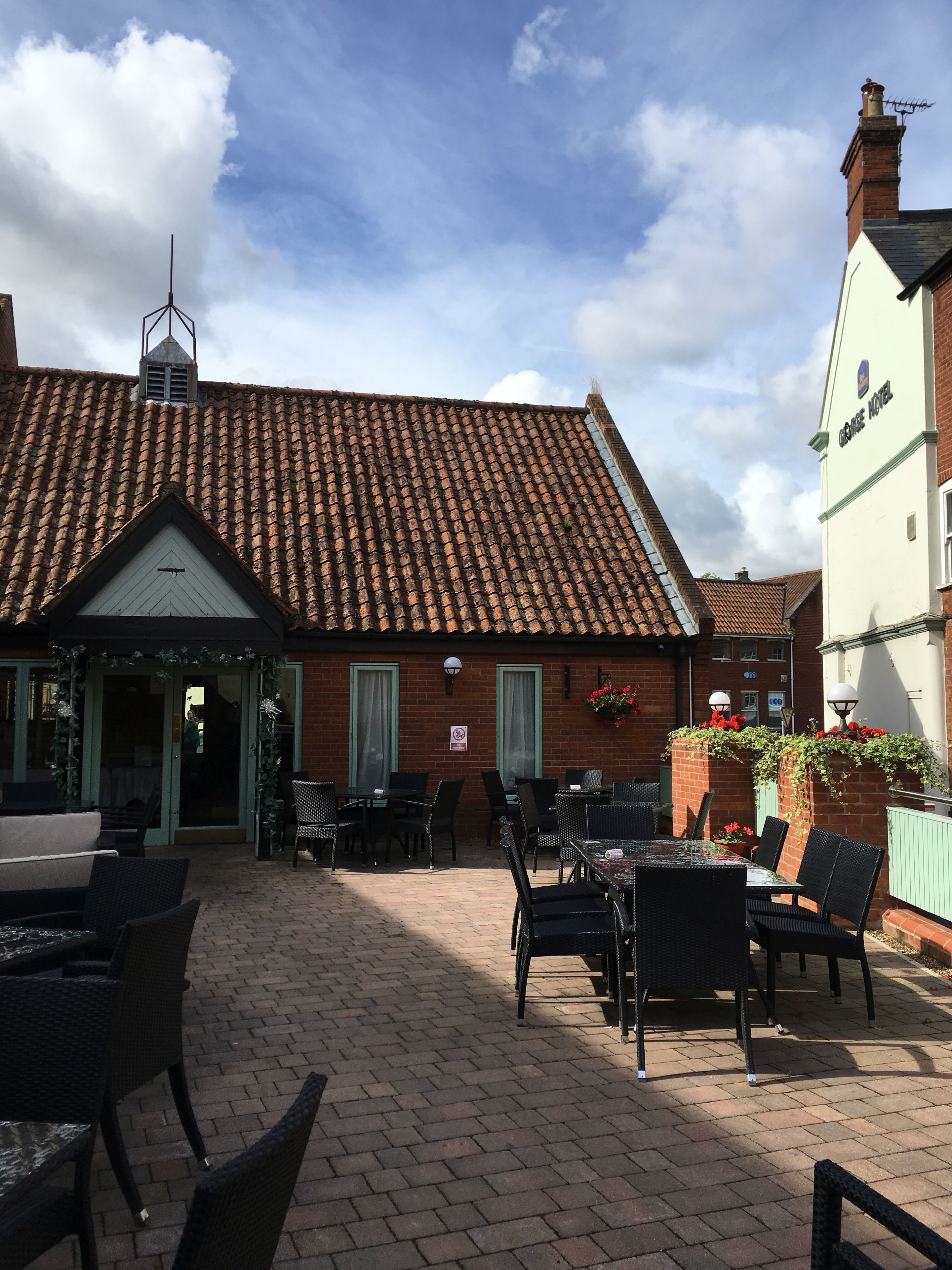 A courtyard with outdoor seating, a brick building with a tiled roof, and a sign indicating a hotel.