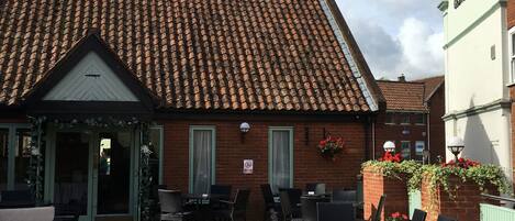 A courtyard with outdoor seating, a brick building with a tiled roof, and a sign indicating a hotel.