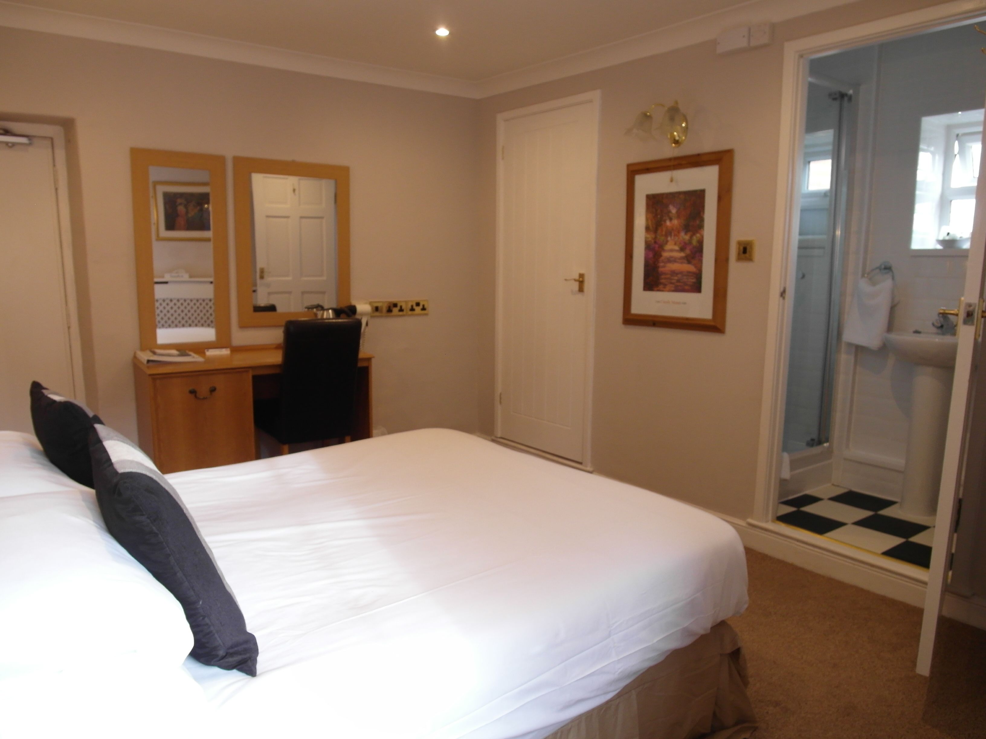 A hotel room with a bed, a desk, a chair, a door, and a bathroom with a shower.