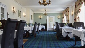 A formal dining room with a plaid carpet, white tablecloths, and black upholstered chairs.