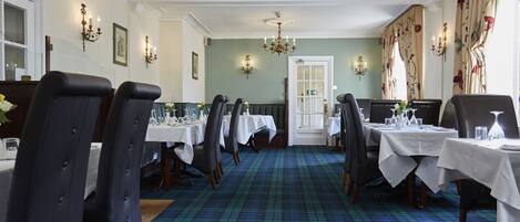 A formal dining room with a plaid carpet, white tablecloths, and black upholstered chairs.