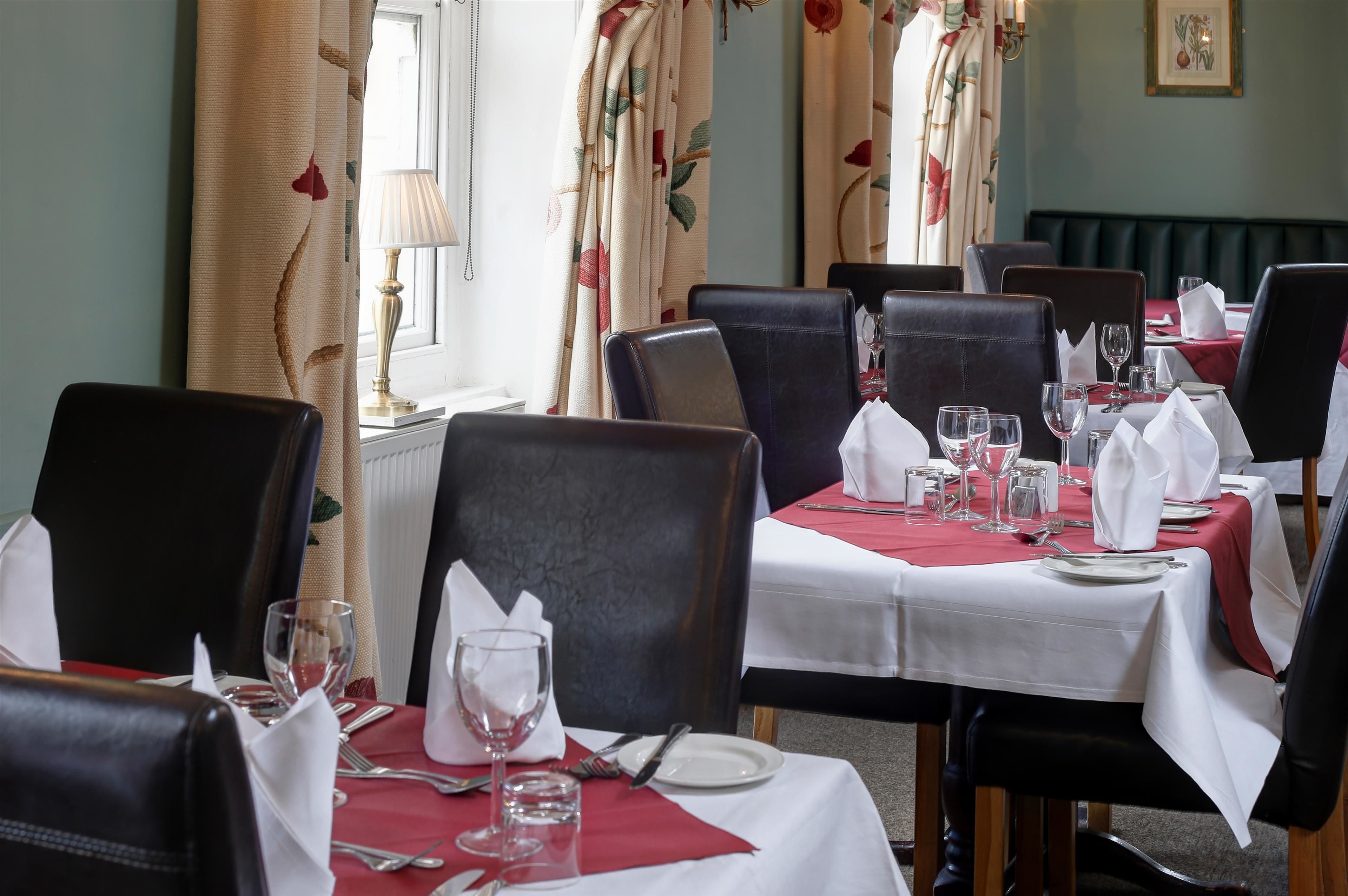 A dining area with tables set for four, each with white tablecloths, black chairs, and neatly arranged cutlery and glassware.