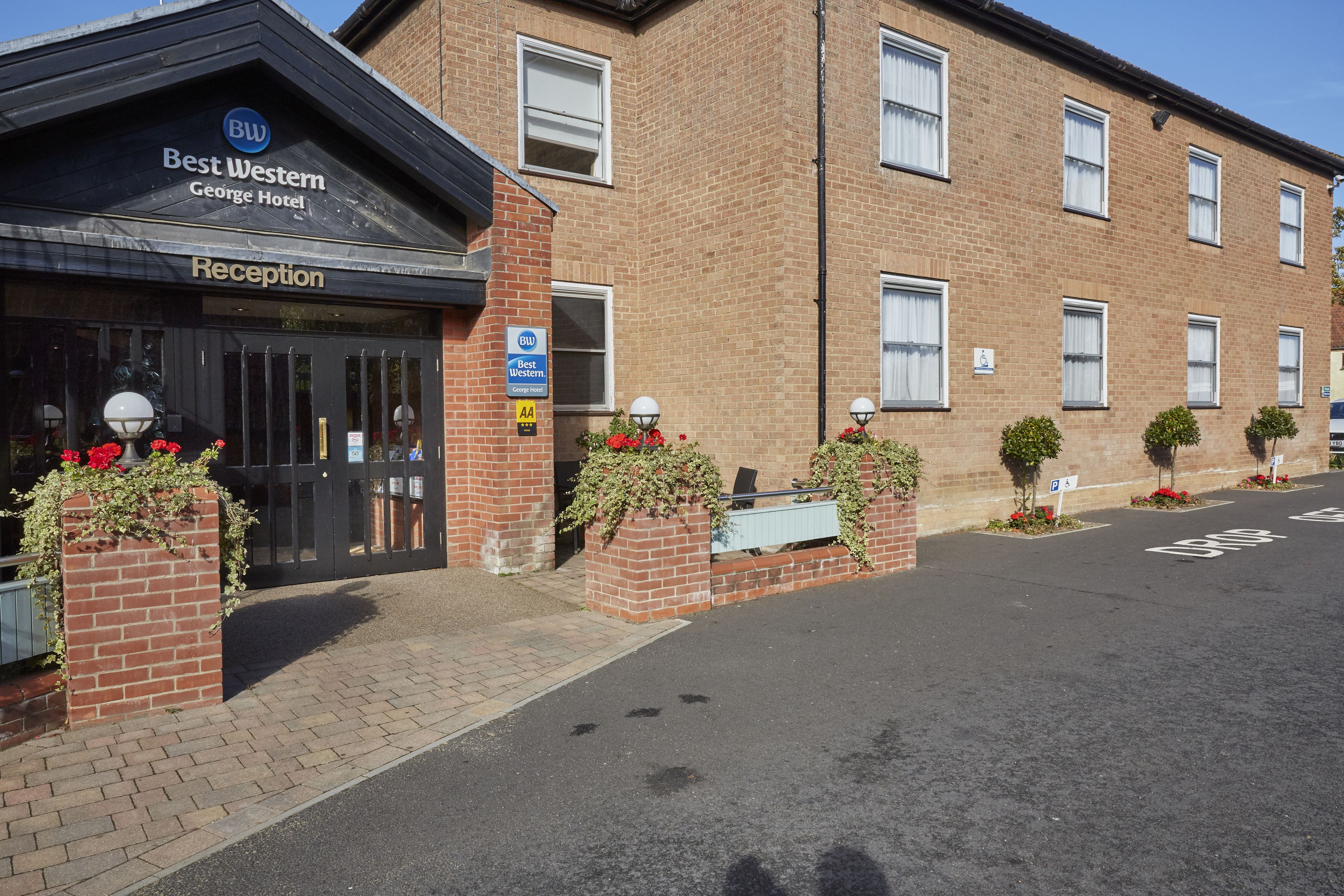 A hotel reception with a clear sign, a brick facade, and a parking area with marked spaces.