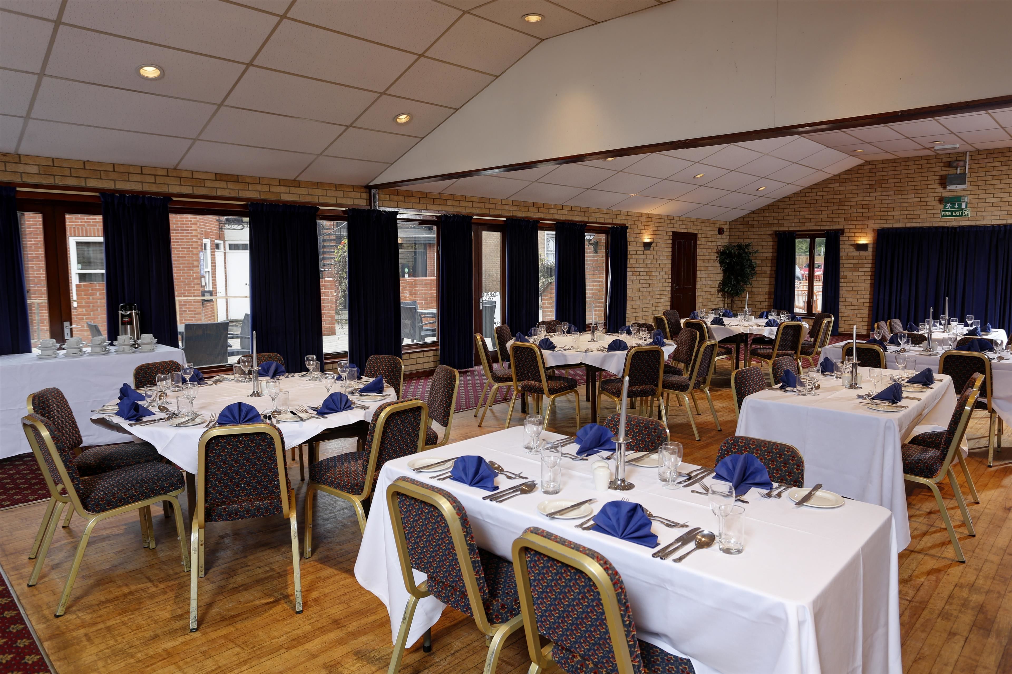 A banquet hall with multiple tables set for dining, featuring white tablecloths, gold chairs, and blue napkins.
