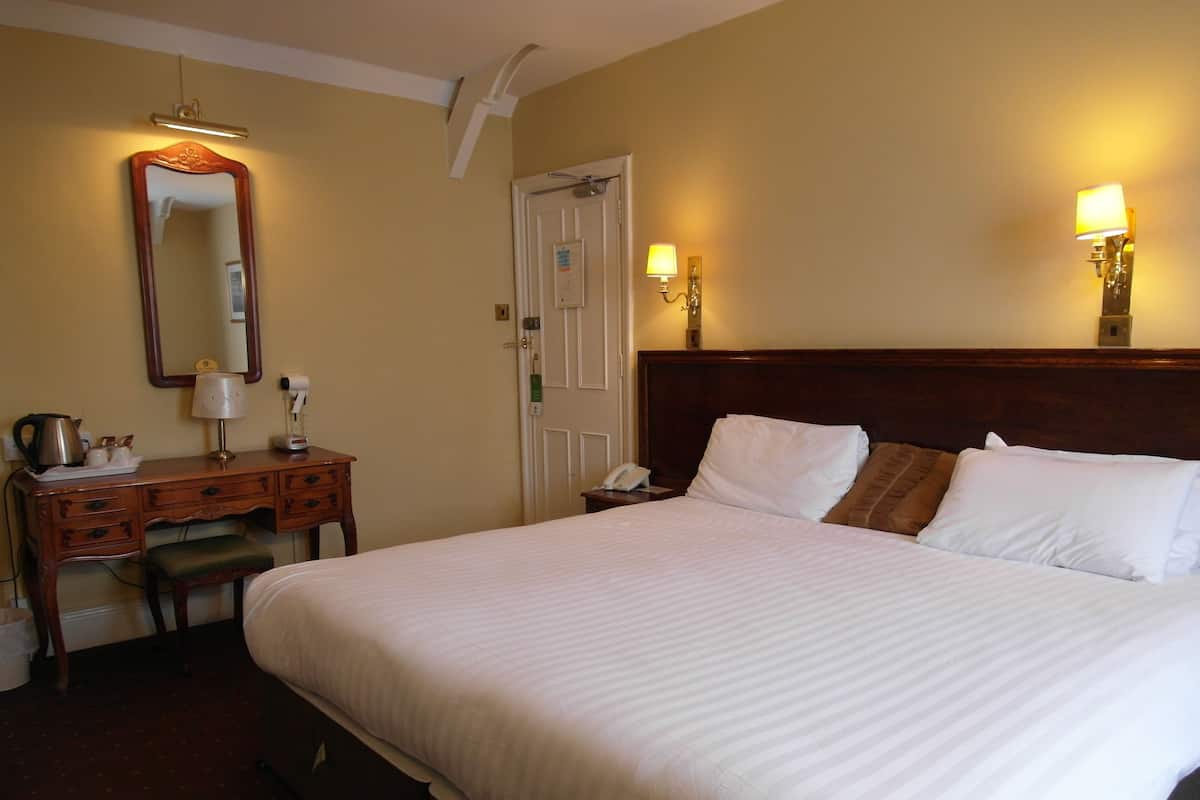 Une chambre d’hôtel avec un grand lit, une commode en bois, un bureau avec une lampe et deux lampes fixées au mur.