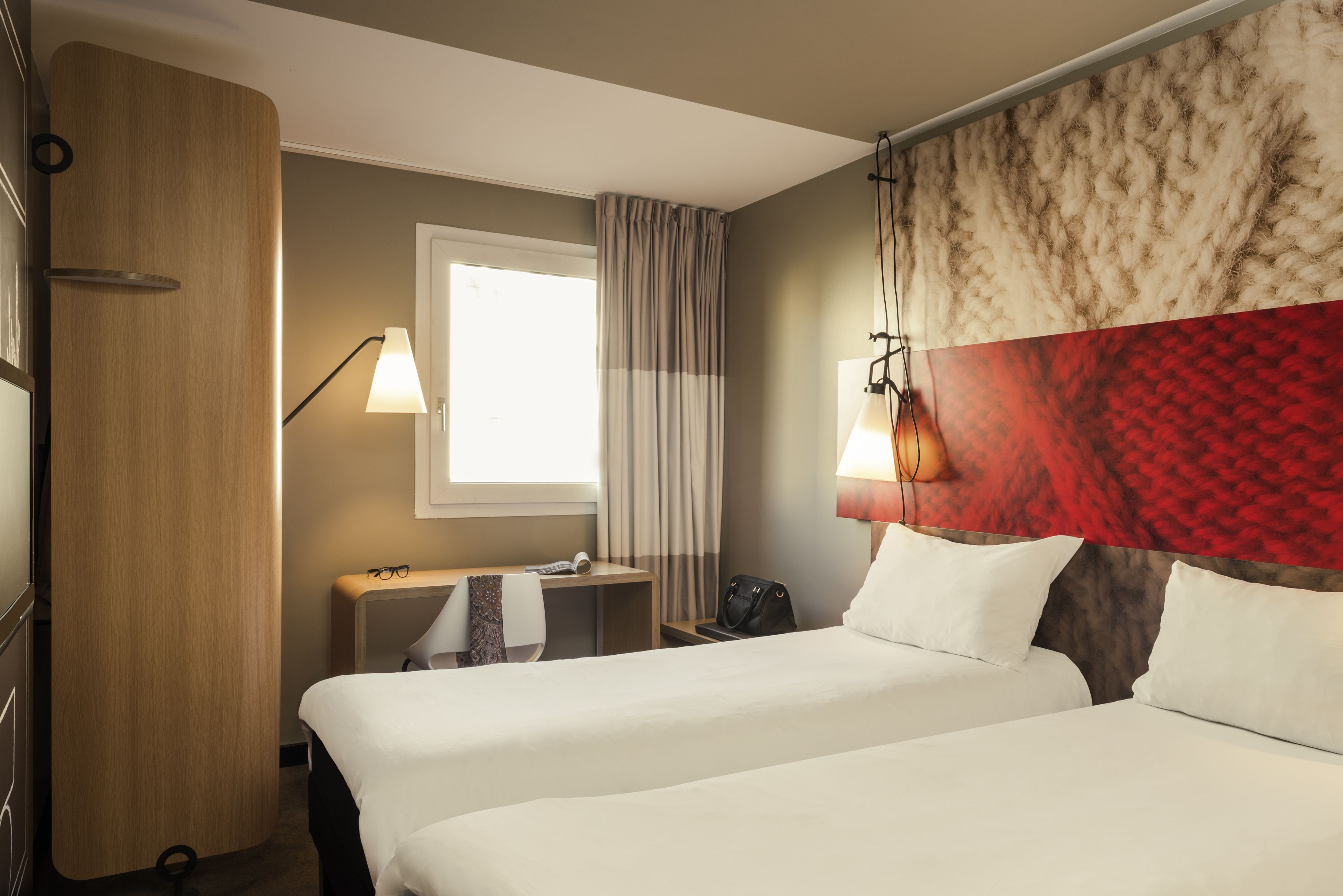 A hotel room with two beds, a desk, a chair, a lamp, and a window with curtains.
