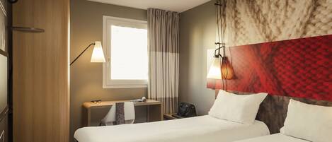 A hotel room with two beds, a desk, a chair, a lamp, and a window with curtains.