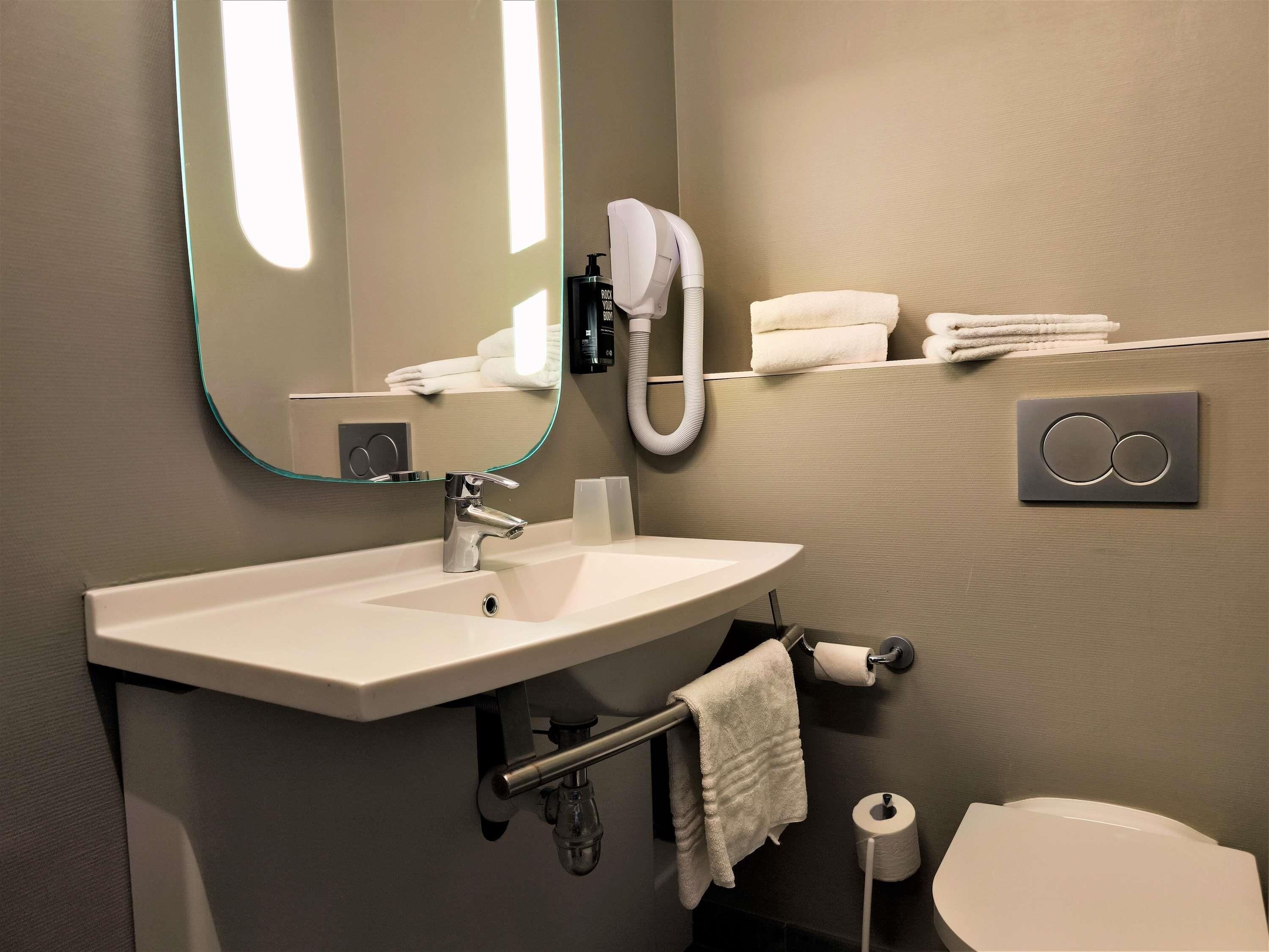 A bathroom with a sink, mirror, towel rack, toilet, and a towel dispenser.