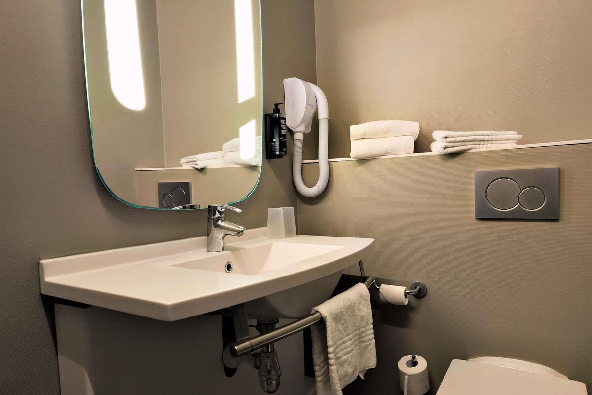 Ein Badezimmer mit Waschbecken, Spiegel, Handtuchhalter, Toilette und Handtuchspender.