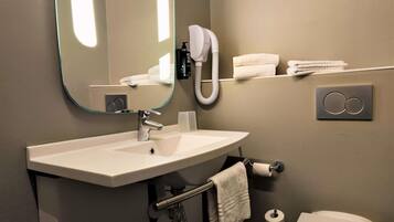 A bathroom with a sink, mirror, towel rack, toilet, and a towel dispenser.