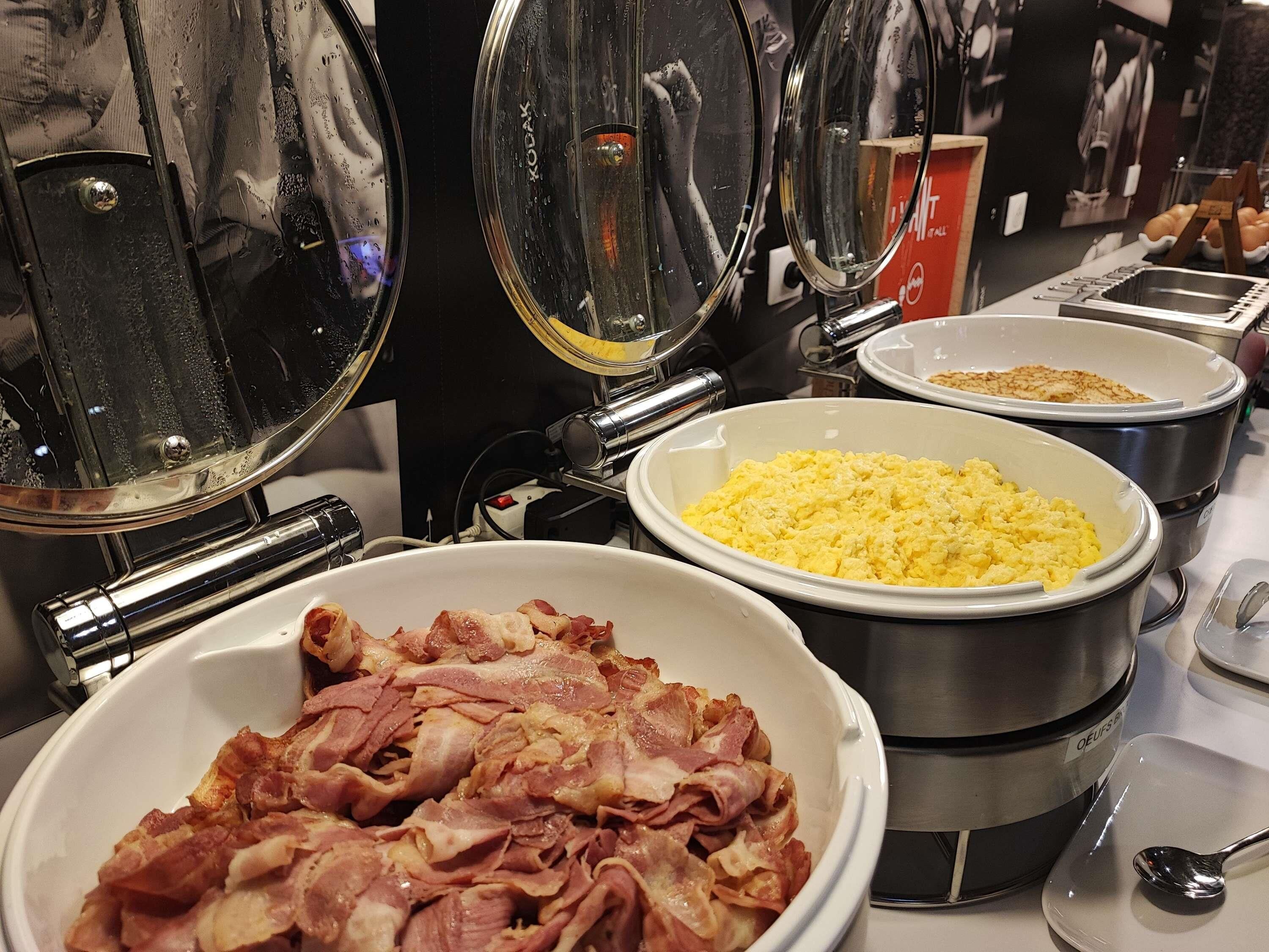 A buffet with various food items including scrambled eggs, bacon, and other dishes in bowls and containers.