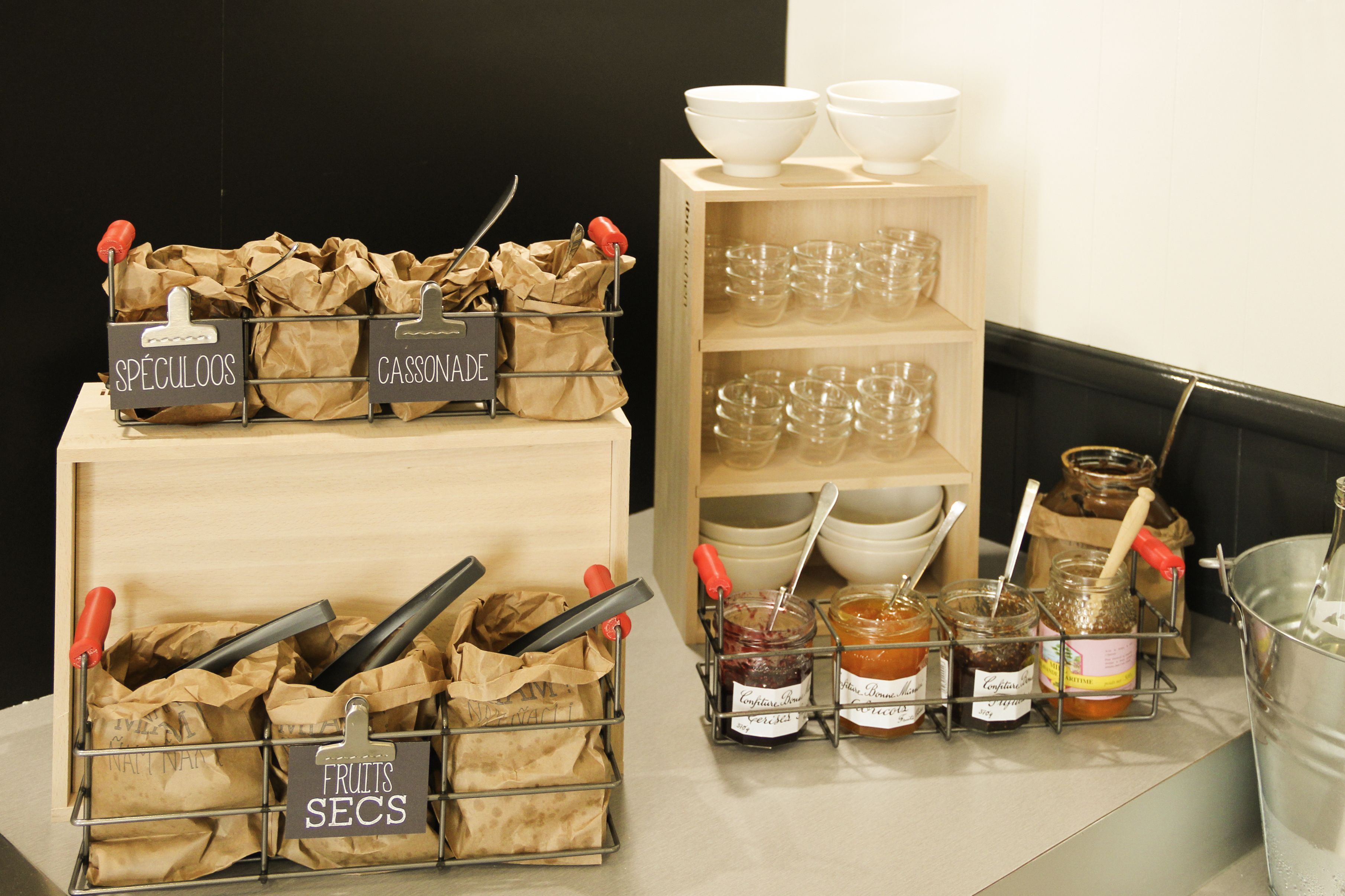 Un área de cocina con recipientes etiquetados para frutas, especias y salsas, además de vasos y frascos en estanterías.