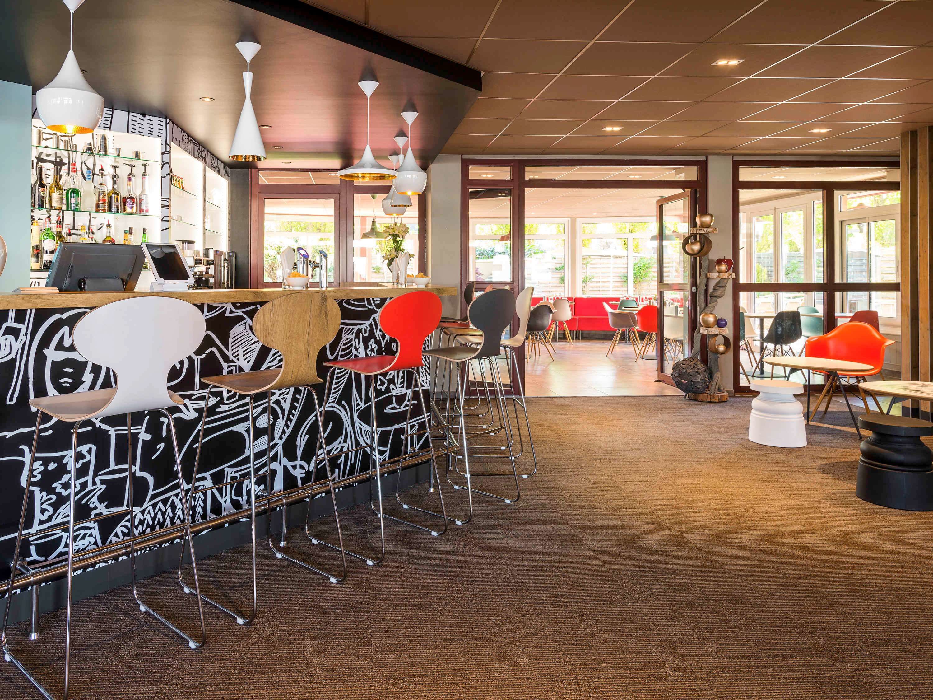 A modern bar area with a patterned wall, multiple seating options including bar stools and chairs, and a variety of hanging pendant lights.