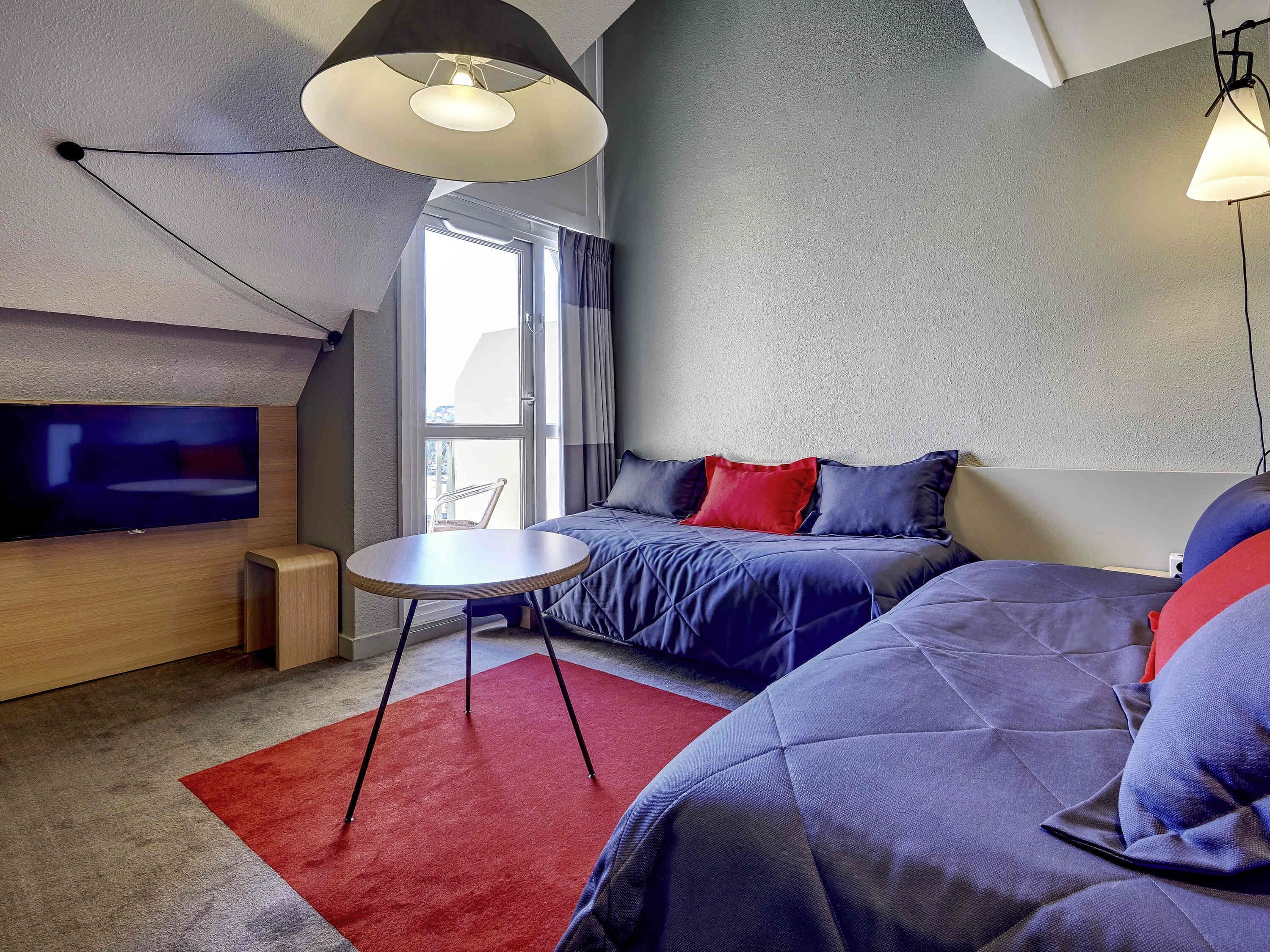 A modern hotel room with a large bed, a TV, a small table, and a red rug.