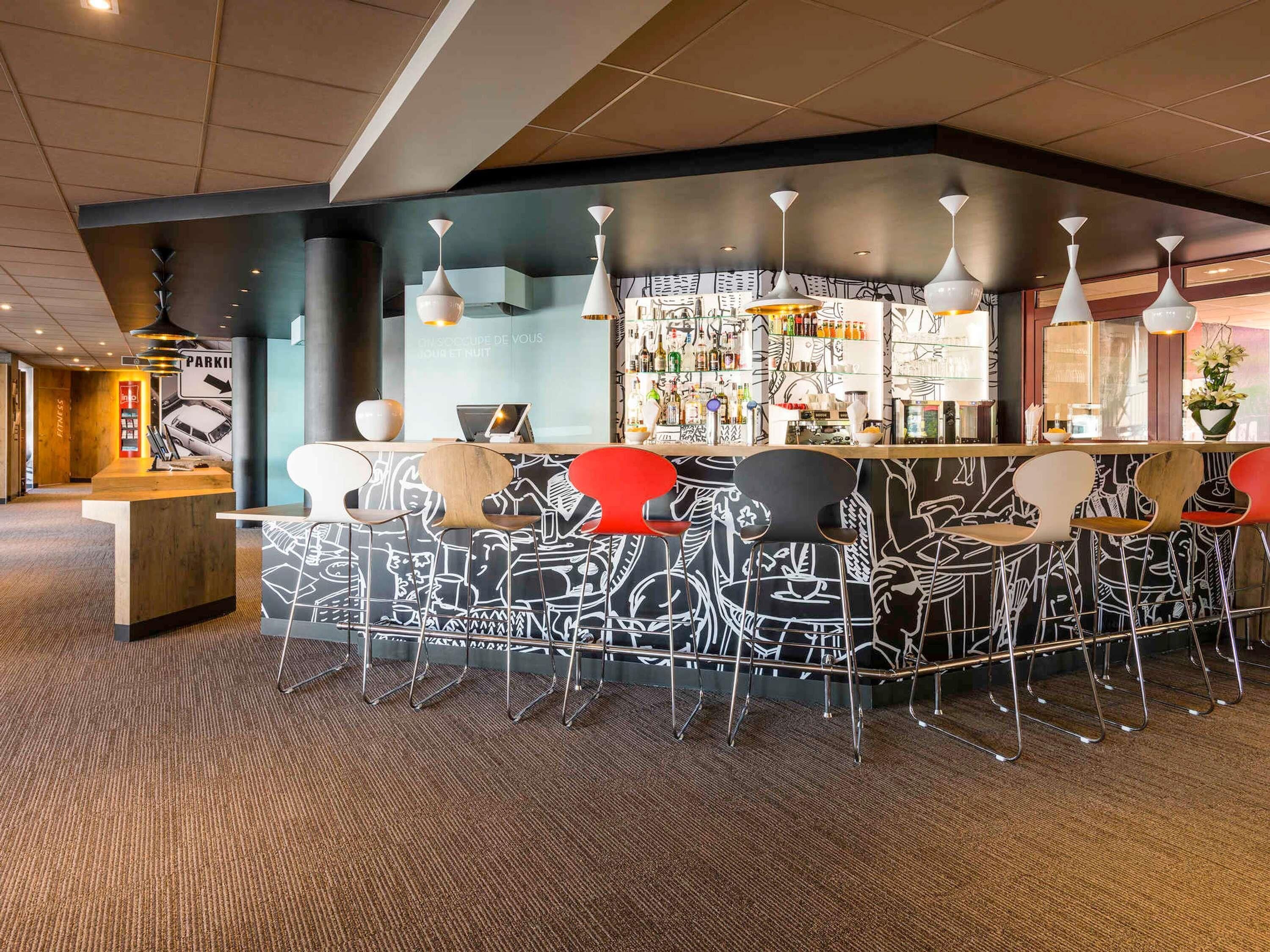A bar area with a counter, multiple chairs, and a wall with a black and white abstract design.