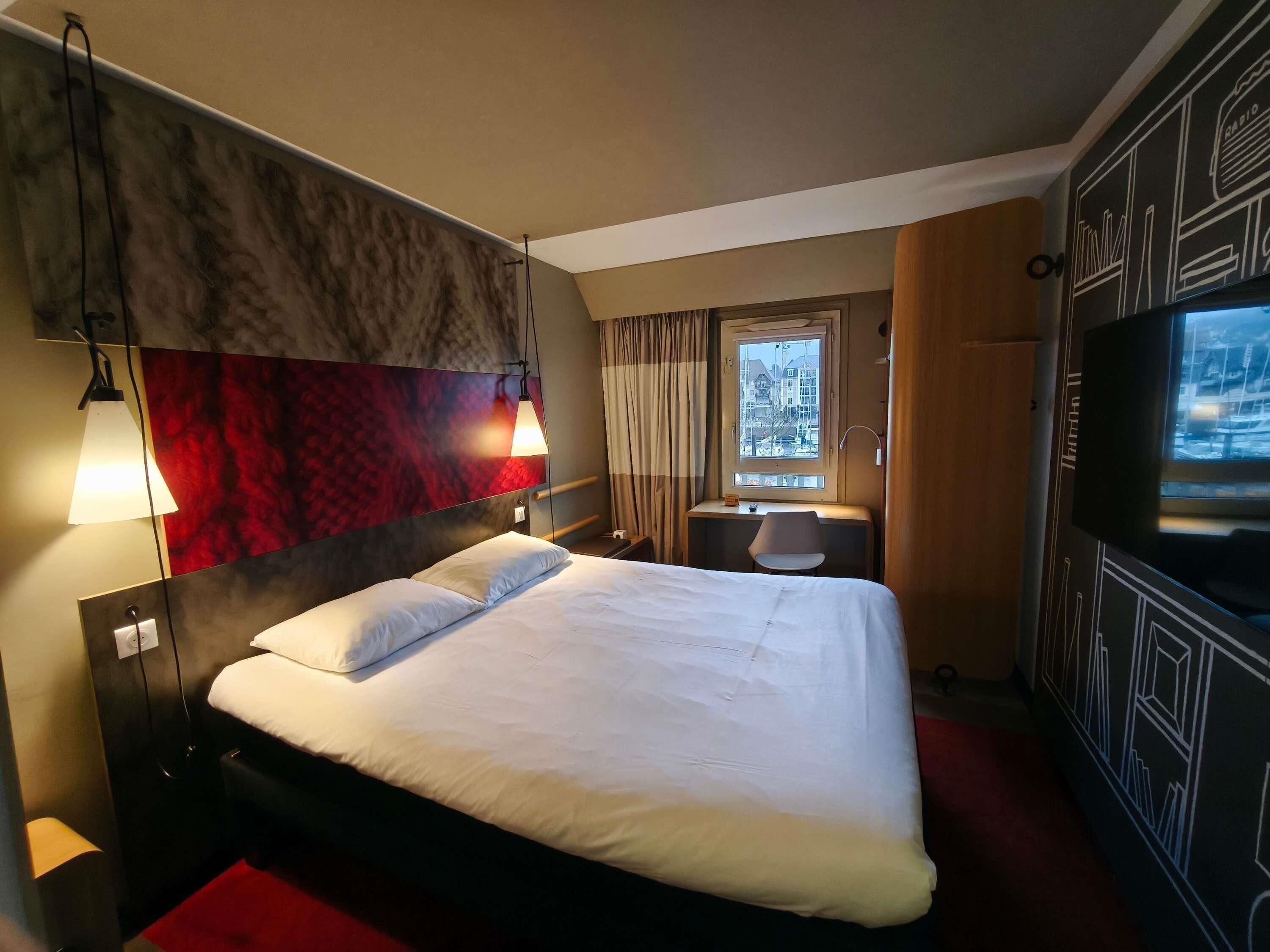 Habitación de hotel con cama, escritorio, silla, televisor y ventana con vista a la ciudad.