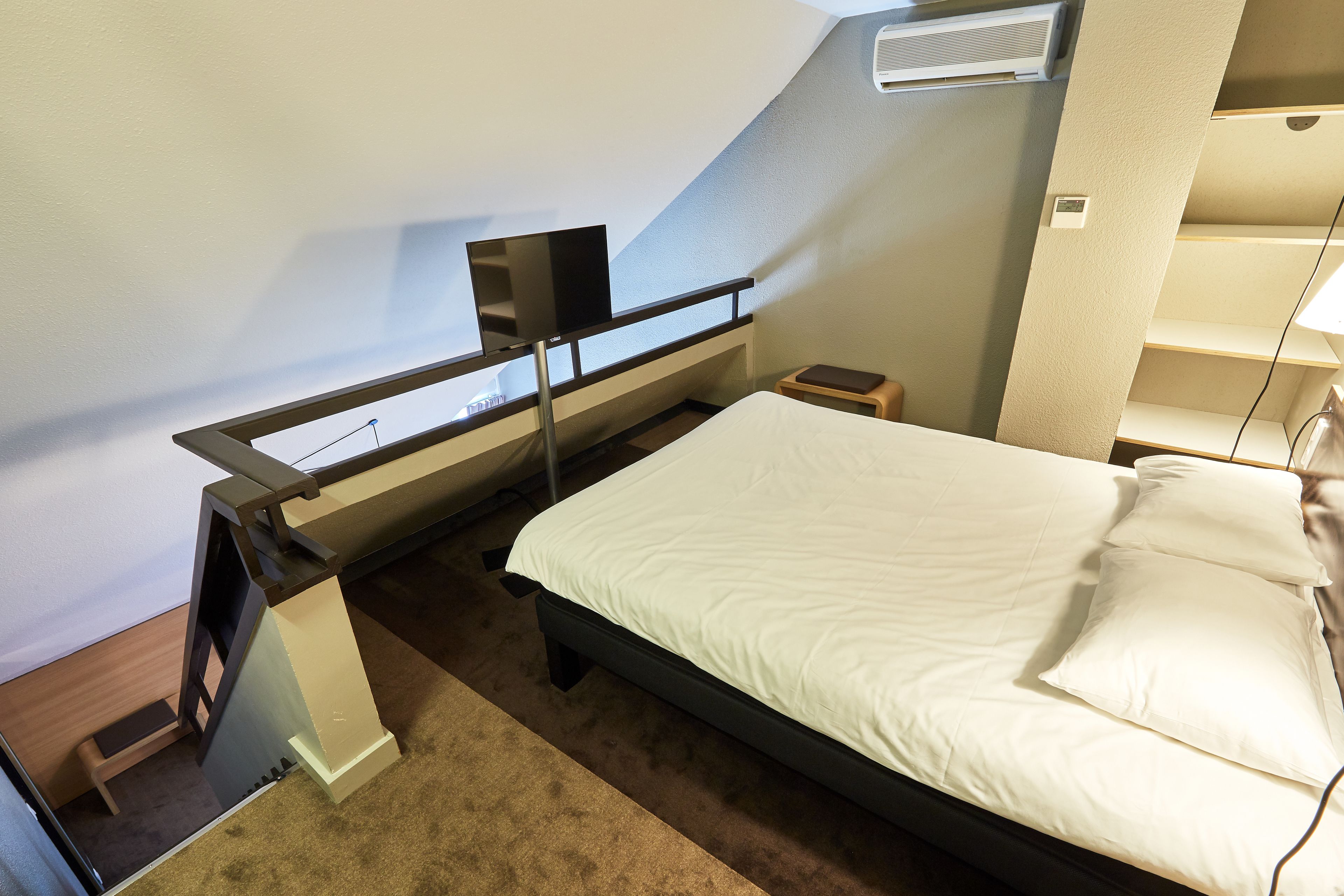 Une petite chambre avec un lit simple, un bureau, une chaise, une petite table et un climatiseur fixé au mur.