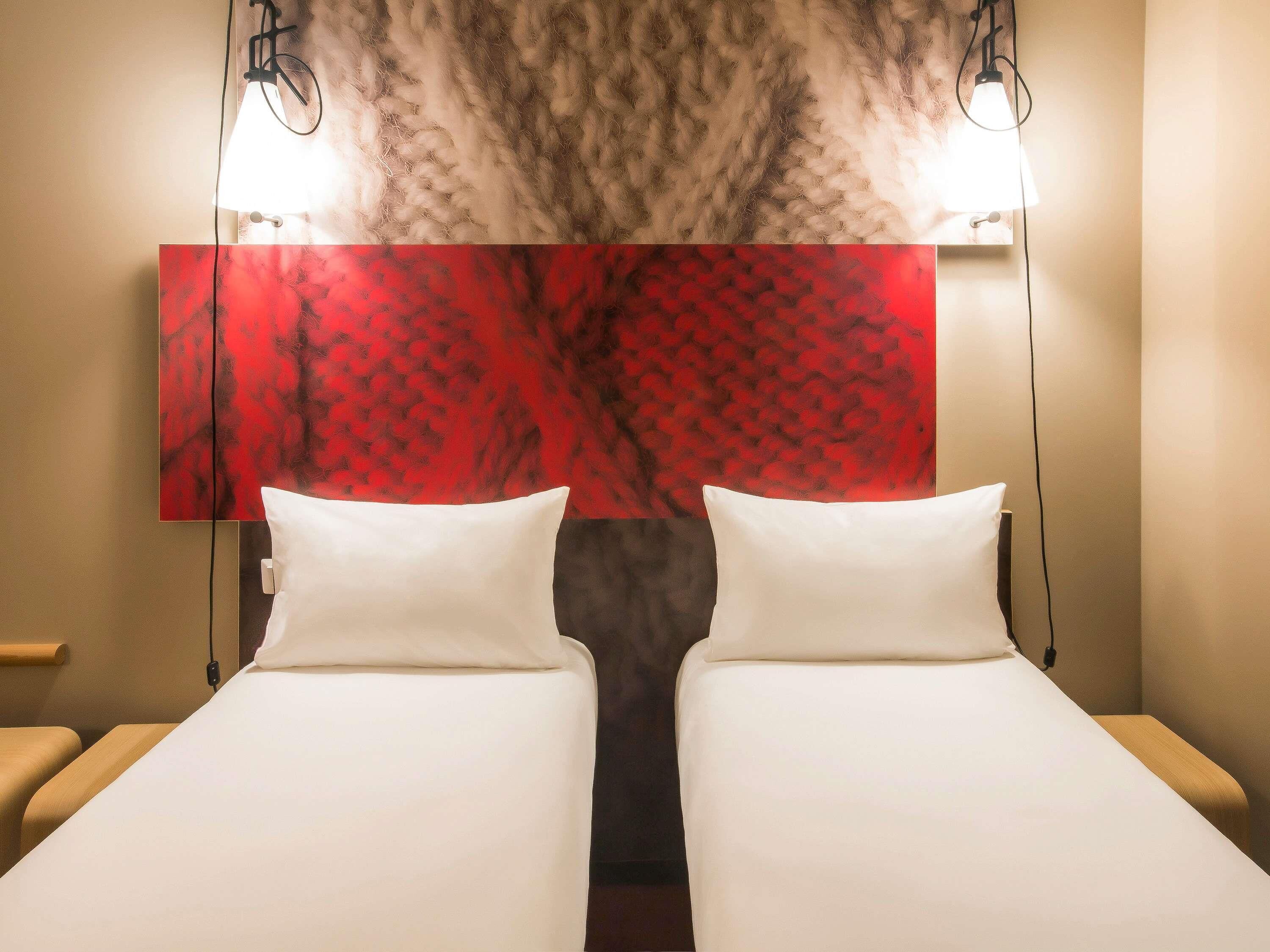 Una habitació d'hotel amb dos llits, una obra d'art abstracta vermella i dues làmpades de nit.