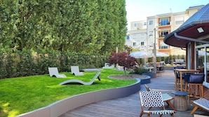 Une terrasse dotée de chaises longues et de tables, entourée d’une pelouse bien entretenue et de haies.