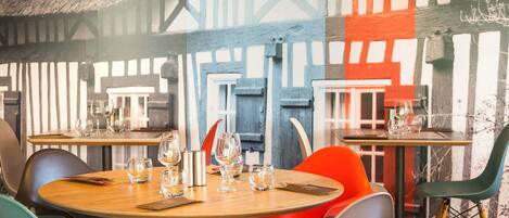 A restaurant interior with round tables, chairs, and a mural on the wall.