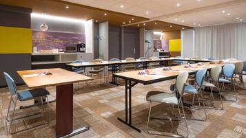 A conference room with multiple tables and chairs, a kitchenette, and a view of the cityscape through the windows.