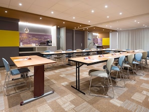 Une salle de conférence équipée de tables, de chaises et d’un coin cuisine.