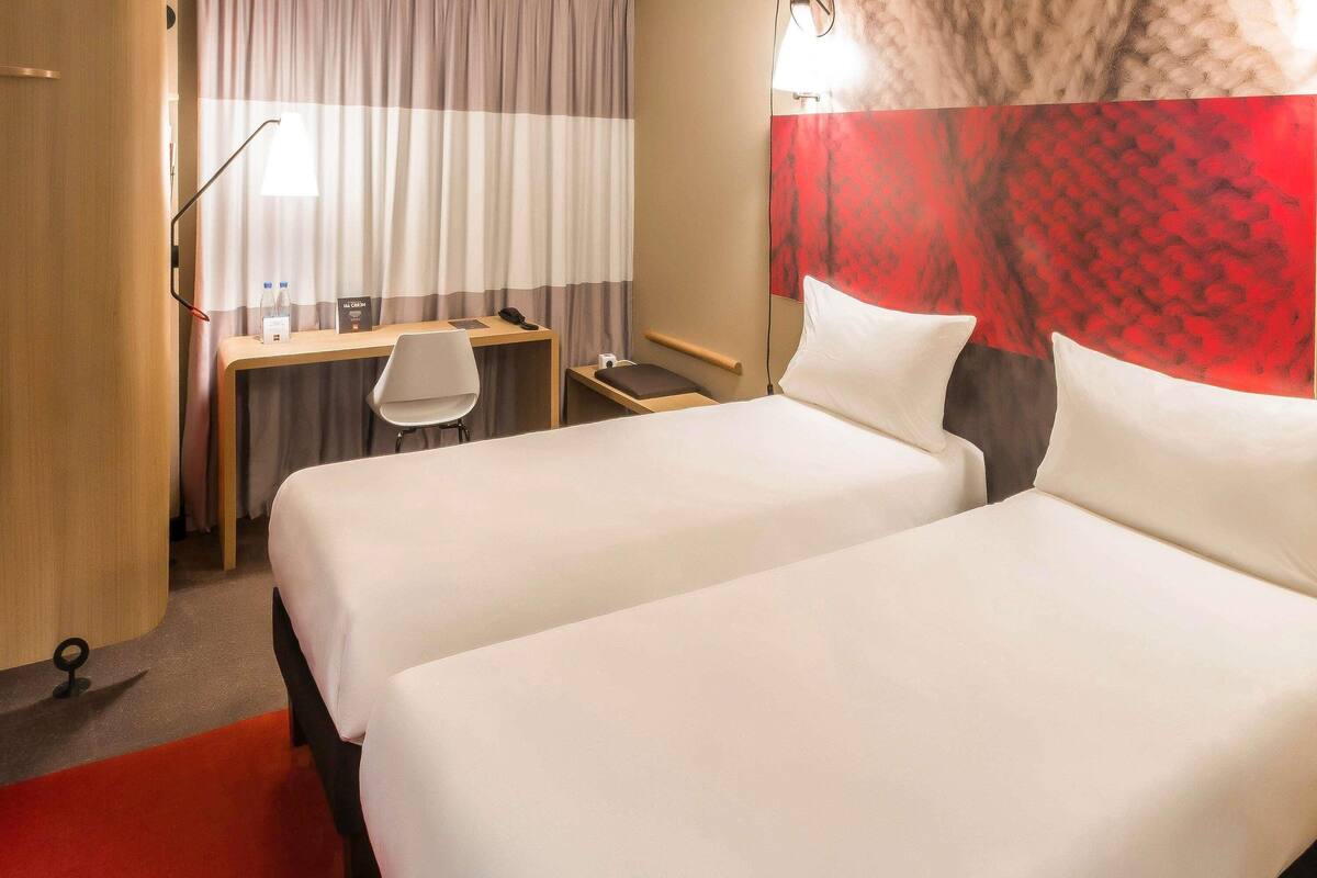Ein Hotelzimmer mit zwei Betten, einem Schreibtisch, einem Stuhl und einem roten Teppich.