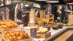 Une vitrine de boulangerie présentant des pâtisseries, une machine à café et une enseigne indiquant « LA MADELEINE ».