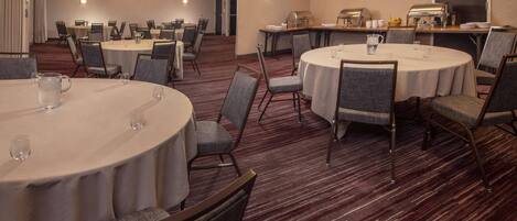 A conference room with round tables, chairs, and a coffee station.