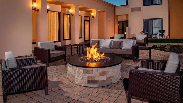 A circular stone fire pit surrounded by wicker furniture and a sofa, with a building in the background. - Sonesta Select Newark Christiana Mall (Newark)